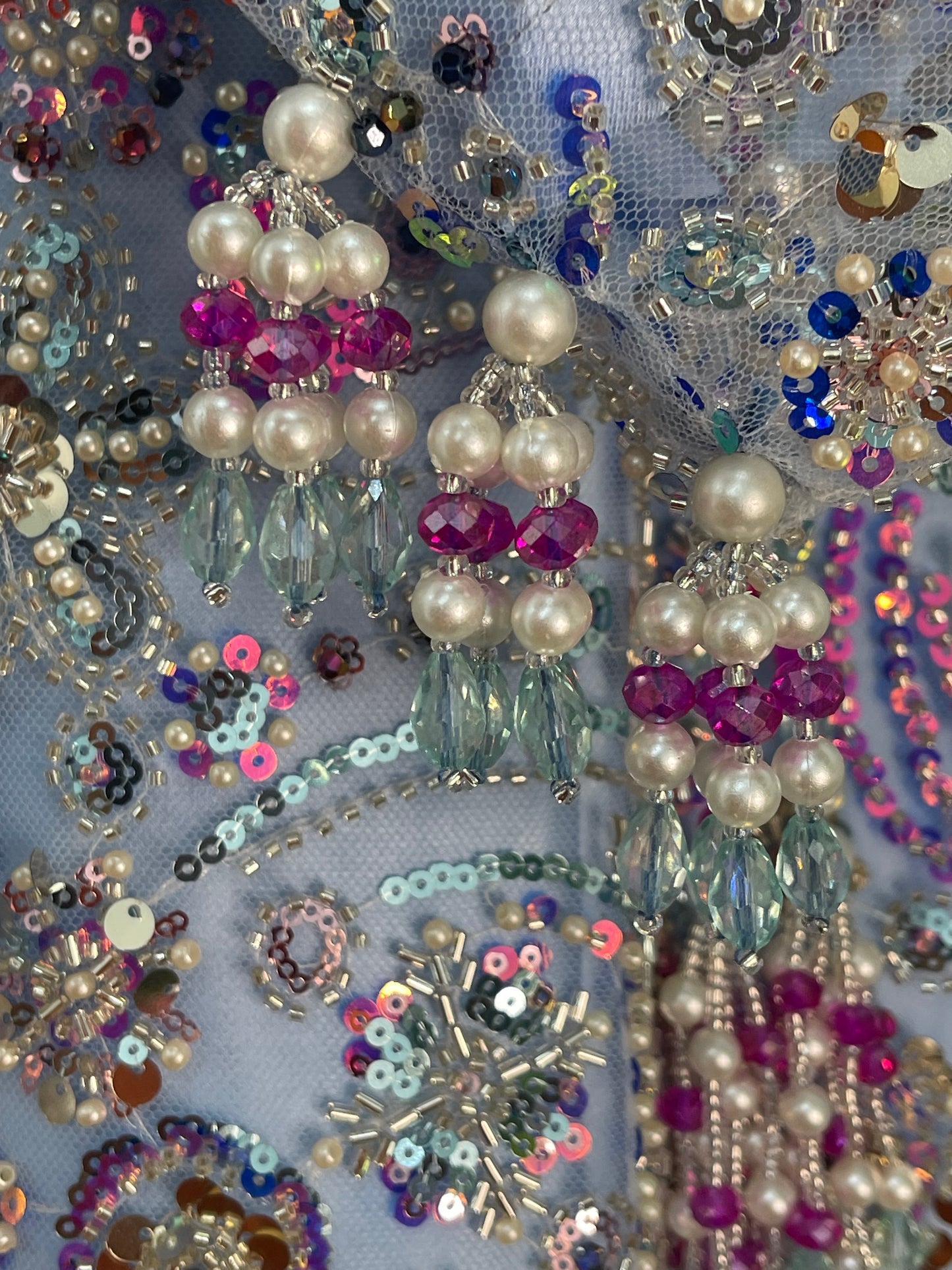 Close-up of decorative fabric with pearls, sequins, and beads on a blue background